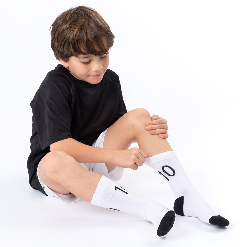 Junge sitzt, zieht Socken an. Weiße Socken mit schwarzem Absatz und der Zahl 10. Schwarzes T-Shirt, weiße Shorts.