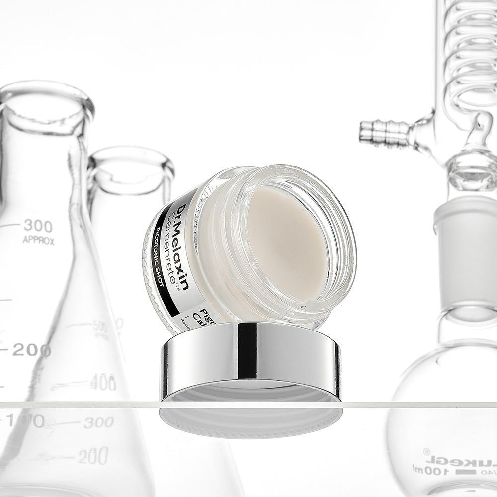 Ein offenes Glas mit weißer Creme steht auf seinem Deckel, umgeben von Laborgeräten.