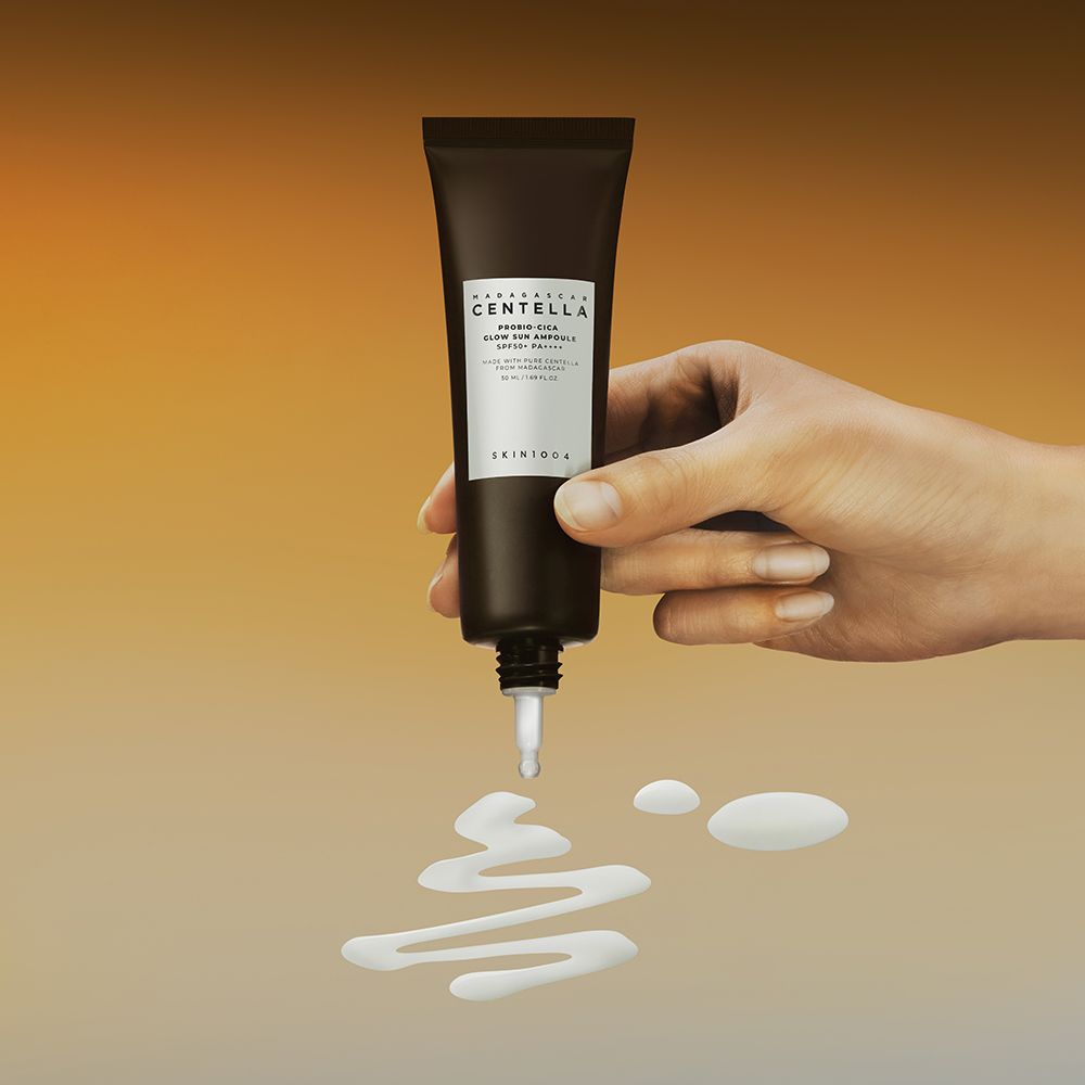 Hand hält Tube. Produkt tropft. Text: MADAGASCAR CENTELLA, PROBIO-CICA GLOW SUN AMPULLE SPF50+ PA++++. Gelbe Tropfen.