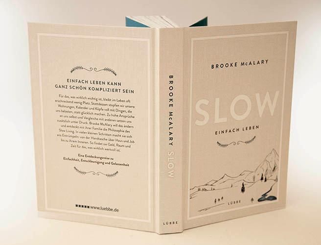 Offenes Buch "SLOW Einfach Leben". Auf der linken Seite Text, rechts Cover-Design mit Bergen und Bäumen. Verlag: Lübbe.