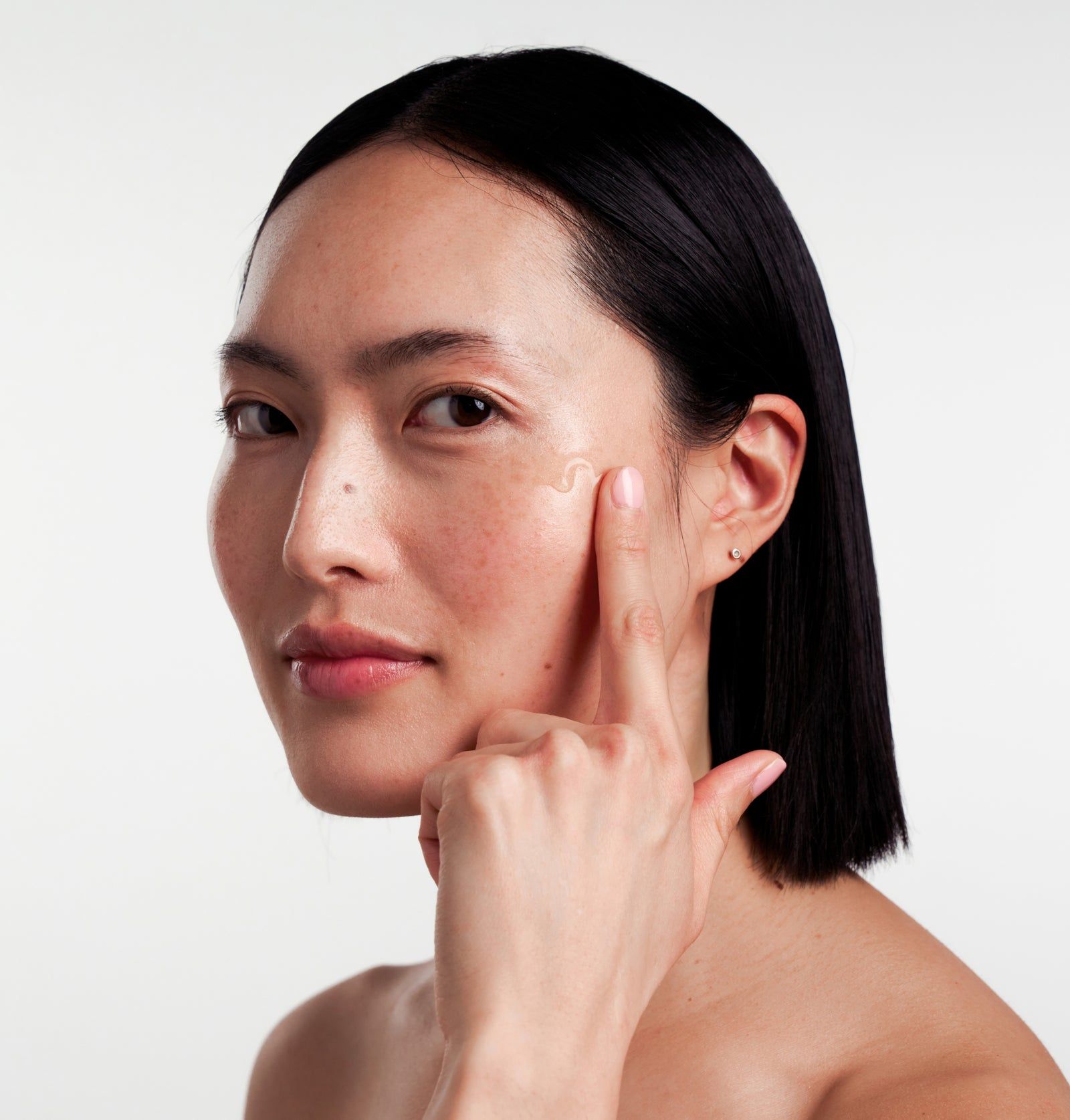 Frau berührt mit dem Finger Serum auf der Wange. Haut mit Serum-Tropfen.