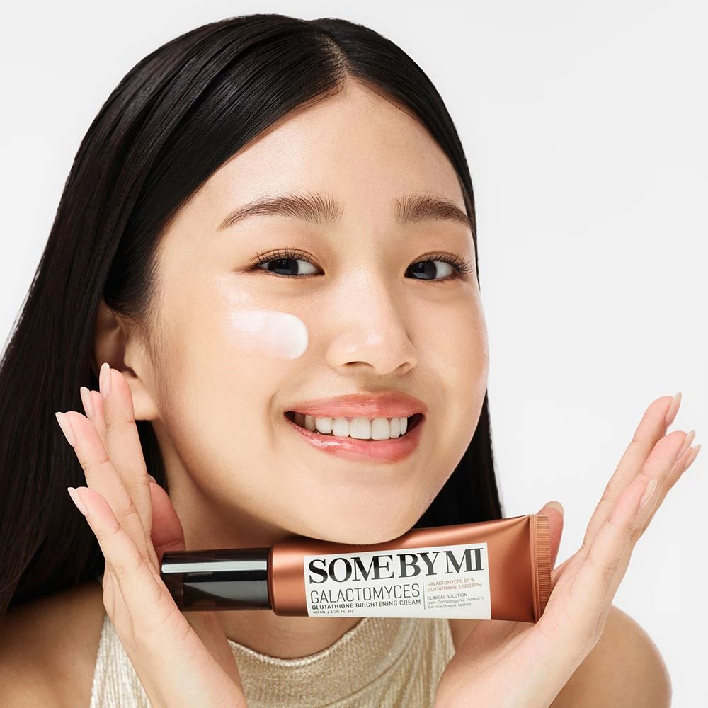 Frau hält Tube SOME BY MI Galactomyces Glutathione Brightening Cream. Creme auf Wange.