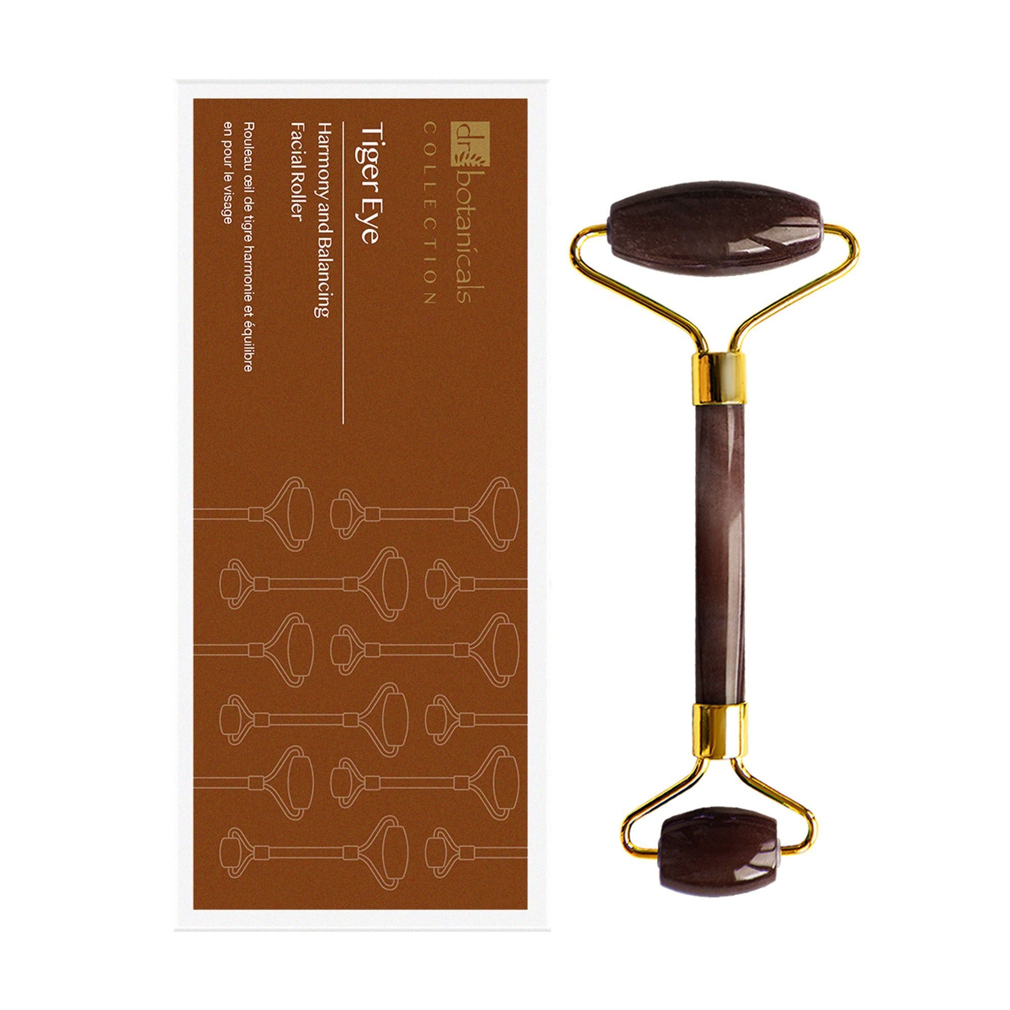 Gesichtsroller und Verpackung. Die Verpackung ist braun mit Produktnamen und Logo. Der Roller hat einen goldenen Griff und braune Rollen.