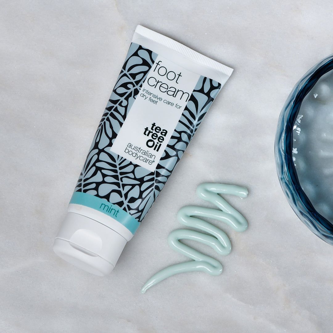Fußcreme-Tube und Klecks Creme. Aufschrift: "foot cream", "tea tree oil", "mint", "australian bodycare". Creme in Wellenform.