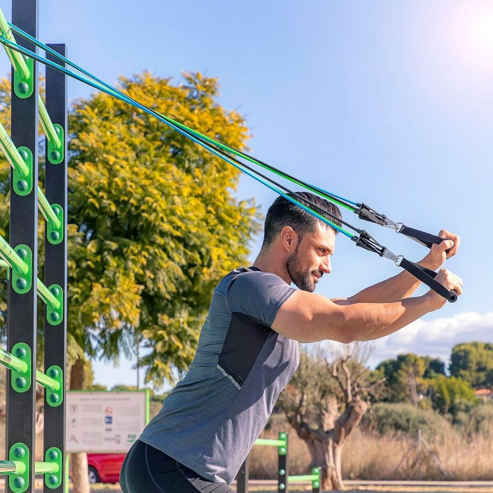 Mann trainiert im Freien mit Widerstandsbändern. Griffe und Bänder in verschiedenen Farben. Sportkleidung. Grüne Umgebung.