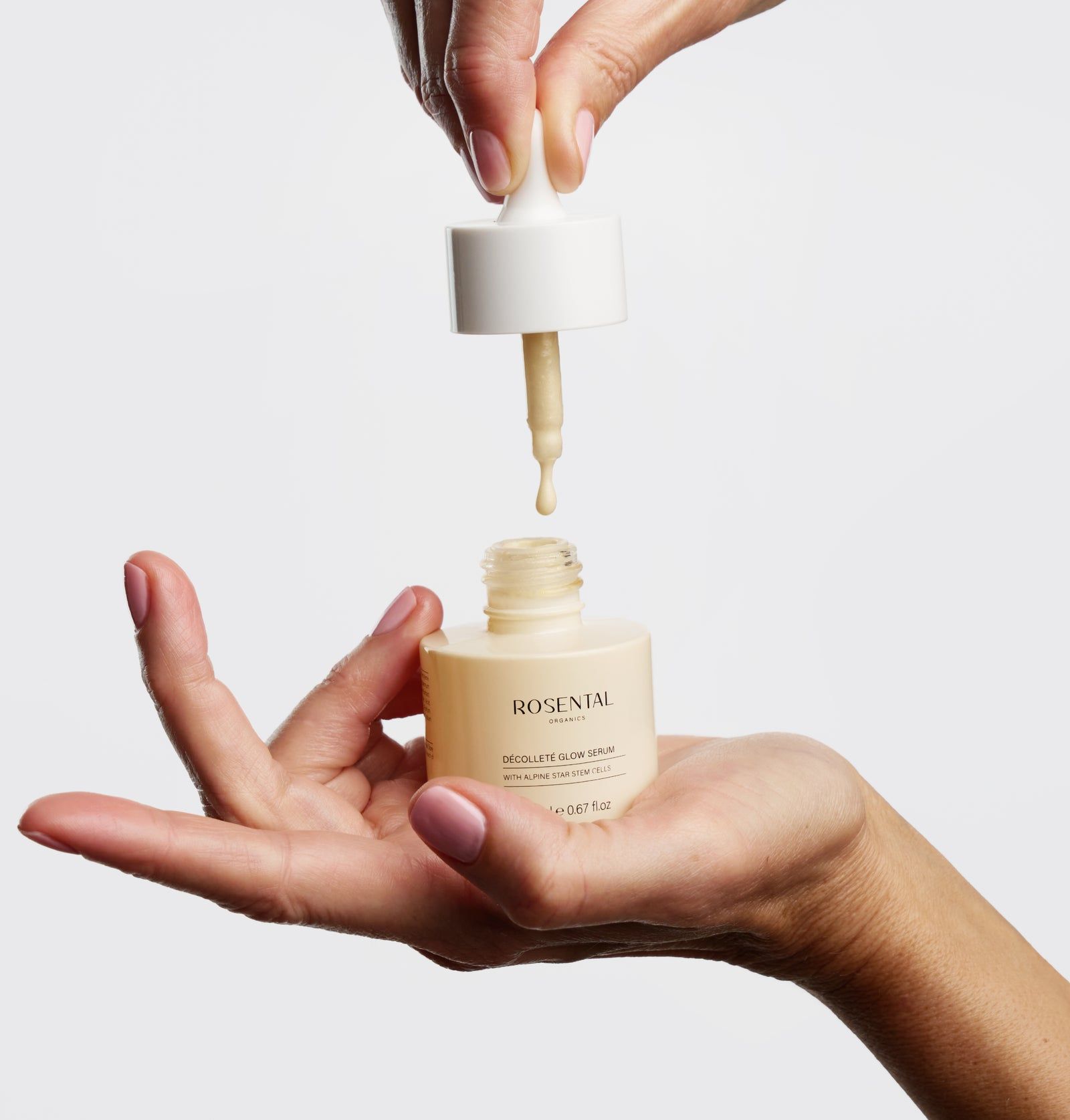 Hände halten eine Serumflasche mit Pipette. Serum tropft in die Flasche. Aufschrift: Rosental Organics Décolleté Glow Serum.