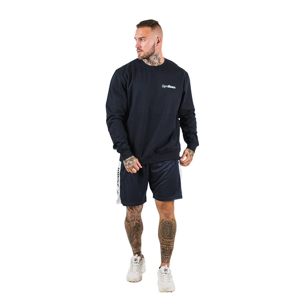 Ein Mann trägt einen dunkelblauen GymBeam Pullover und blaue Shorts. Weißer Hintergrund.