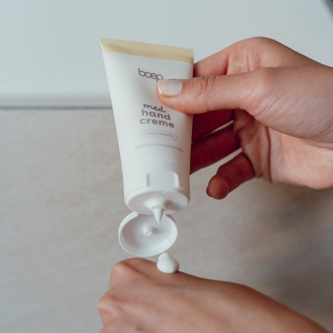 Eine Tube Creme wird auf eine Hand aufgetragen. Die Creme wird aus der Tube gedrückt.