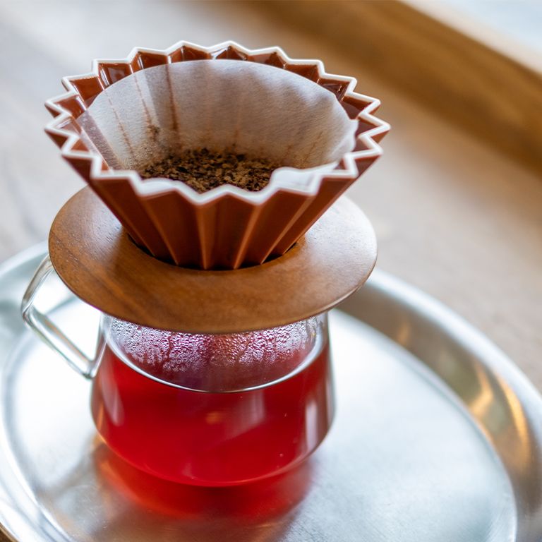 Kaffeefilter mit Kaffeepulver auf einer Glas-Kanne. Auf einer silbernen Untertasse.