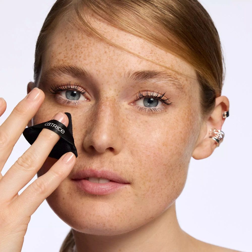 Schwarzes Catrice Powder Puff wird unter dem Auge verwendet. Das Produkt ist dreieckig mit einem schwarzen Band.
