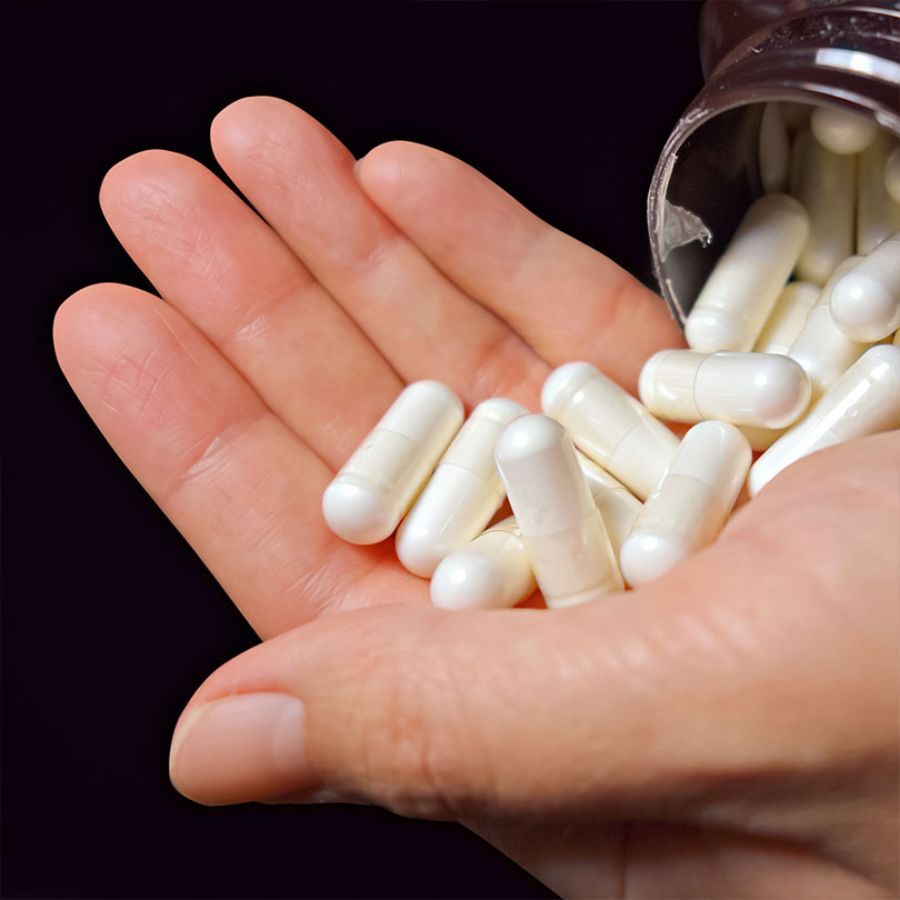 Hand mit weißen Kapseln. Kapseln sind länglich, mit abgerundeten Enden. Produktpräsentation.