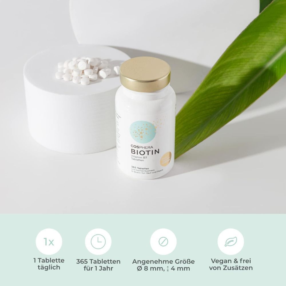 Biotin-Tabletten in einer weißen Flasche. 365 Tabletten für 1 Jahr. Auf einem Podest mit grünen Blättern.