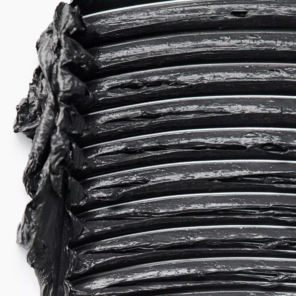 Nahaufnahme von schwarzer Mascara auf einer Oberfläche. Die Textur ist dick und uneben.