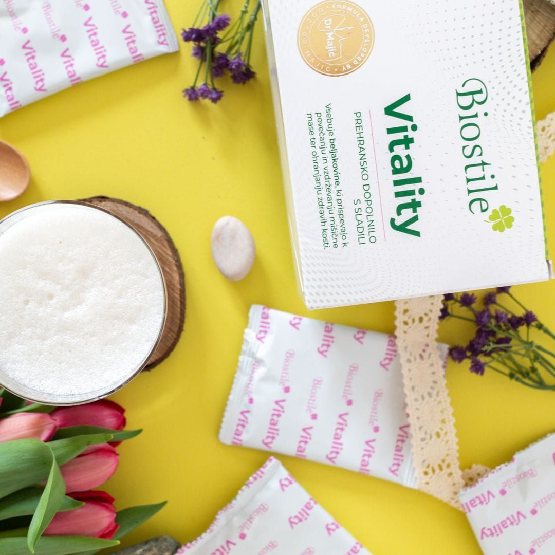 Gelber Hintergrund mit Biostile Vitality-Packungen und -Beuteln. Glas mit Getränk, Blumen und Dekoration. Produktname und Logo deutlich sichtbar.