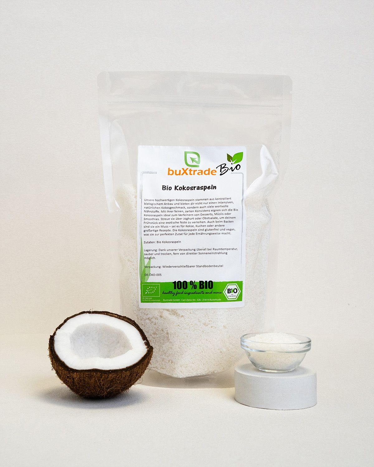Verpackung mit buXtrade Bio Kokosraspeln, halbe Kokosnuss und Schale mit Raspeln. Bio-Siegel.