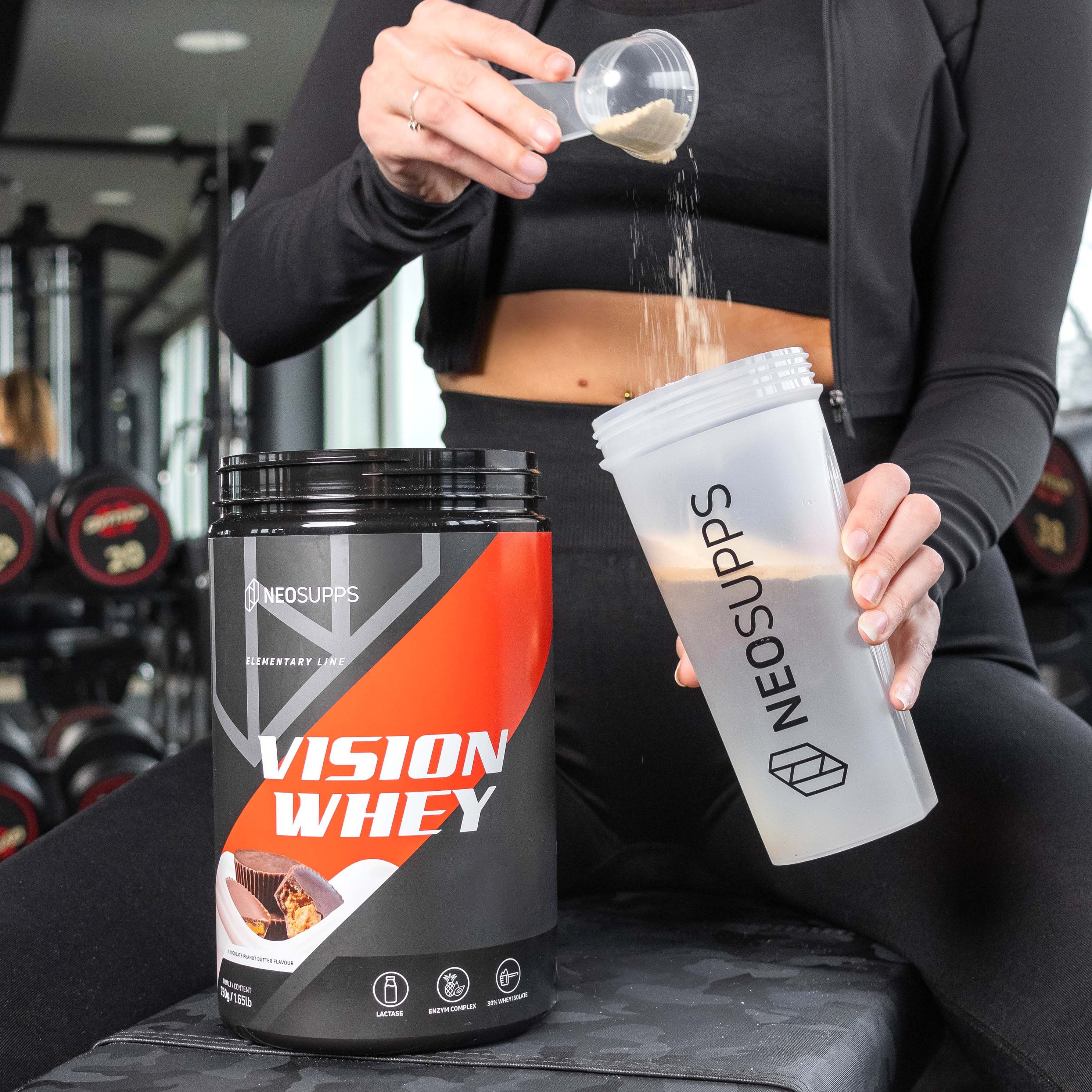 Person gießt Pulver in Shaker. Dose mit Produkt daneben. Aufschrift: Vision Whey. Shaker mit Logo.