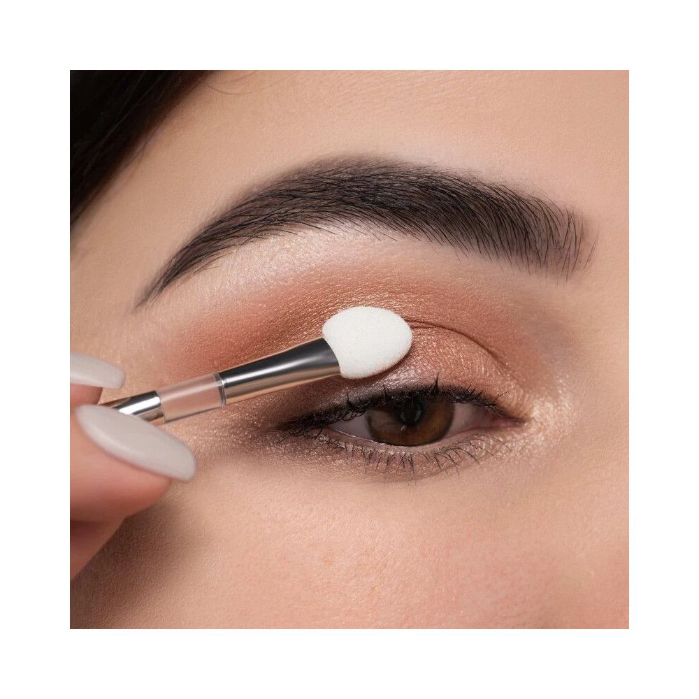 Nahaufnahme eines Auges, das mit einem Lidschattenapplikator geschminkt wird. Helle, ovale Applikatorspitze.