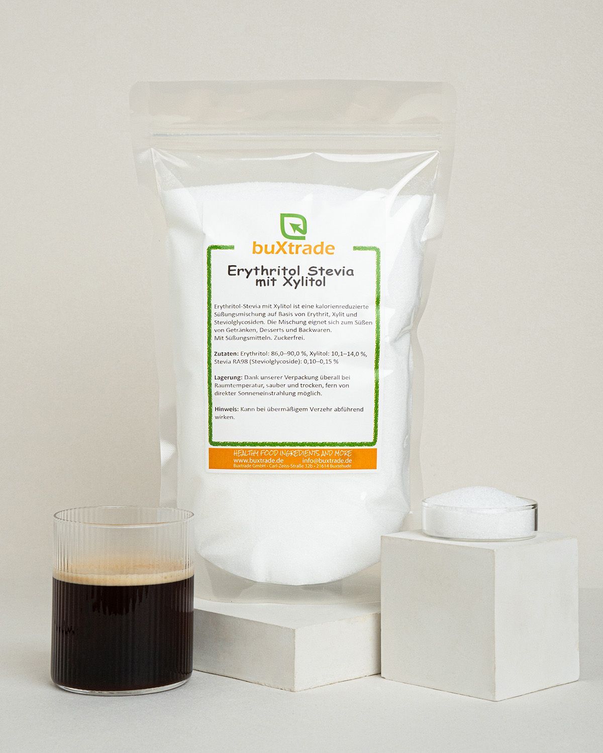 Ein Beutel buxtrade Erythritol Stevia mit Xylitol neben einem Glas Kaffee und einem kleinen Behälter mit Süßstoff.