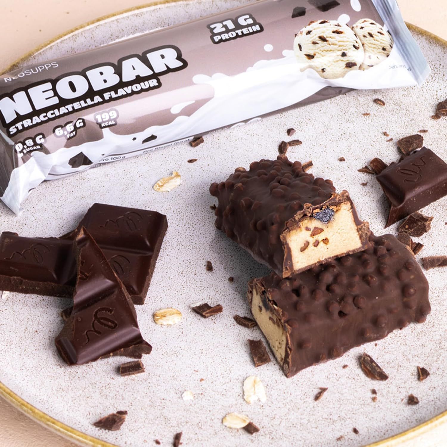 Aufgeschnittene Proteinriegel auf einem Teller. Daneben Schokostücke und die Verpackung. Aufdruck: NEOBAR, 21g Protein, Stracciatella Flavour.