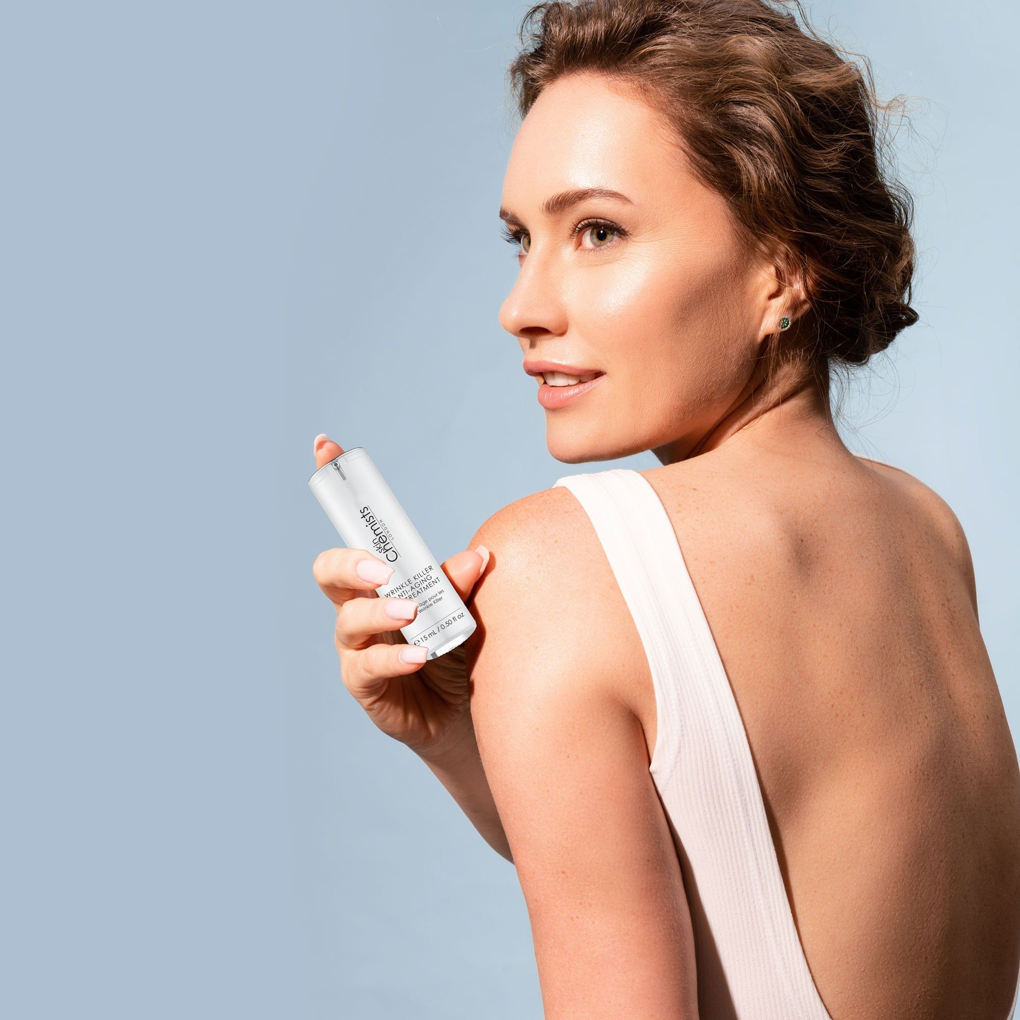 Frau hält zylindrische Augenbehandlung. Weißer Behälter mit silbernem Deckel. Text: Wrinkle Killer Anti-Aging Eye Treatment, 15 ml / 0.50 fl oz.