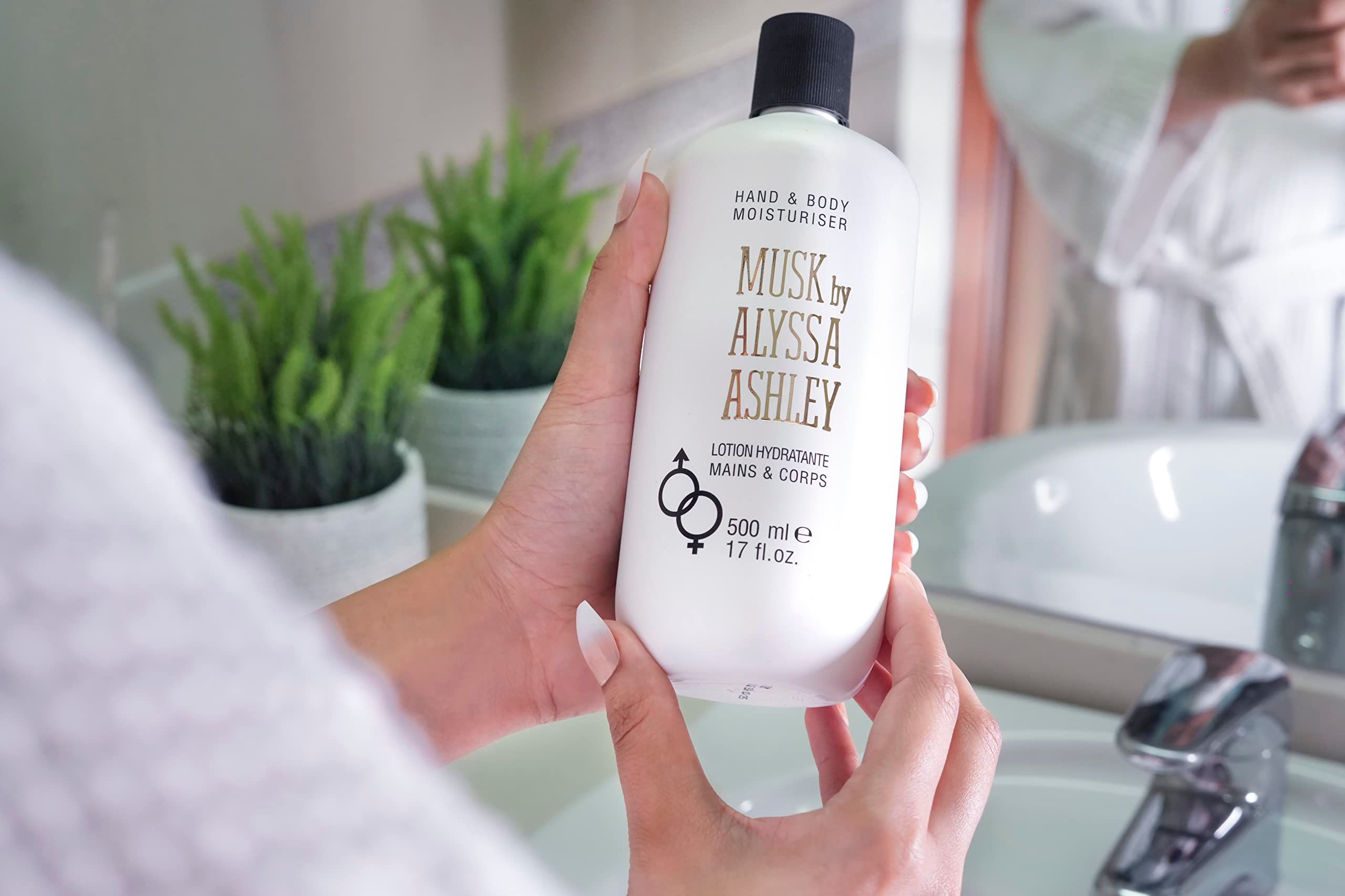 Weiße Flasche mit schwarzem Deckel, gehalten von Händen. Aufschrift: Musk by Alyssa Ashley, Hand & Body Moisturiser.