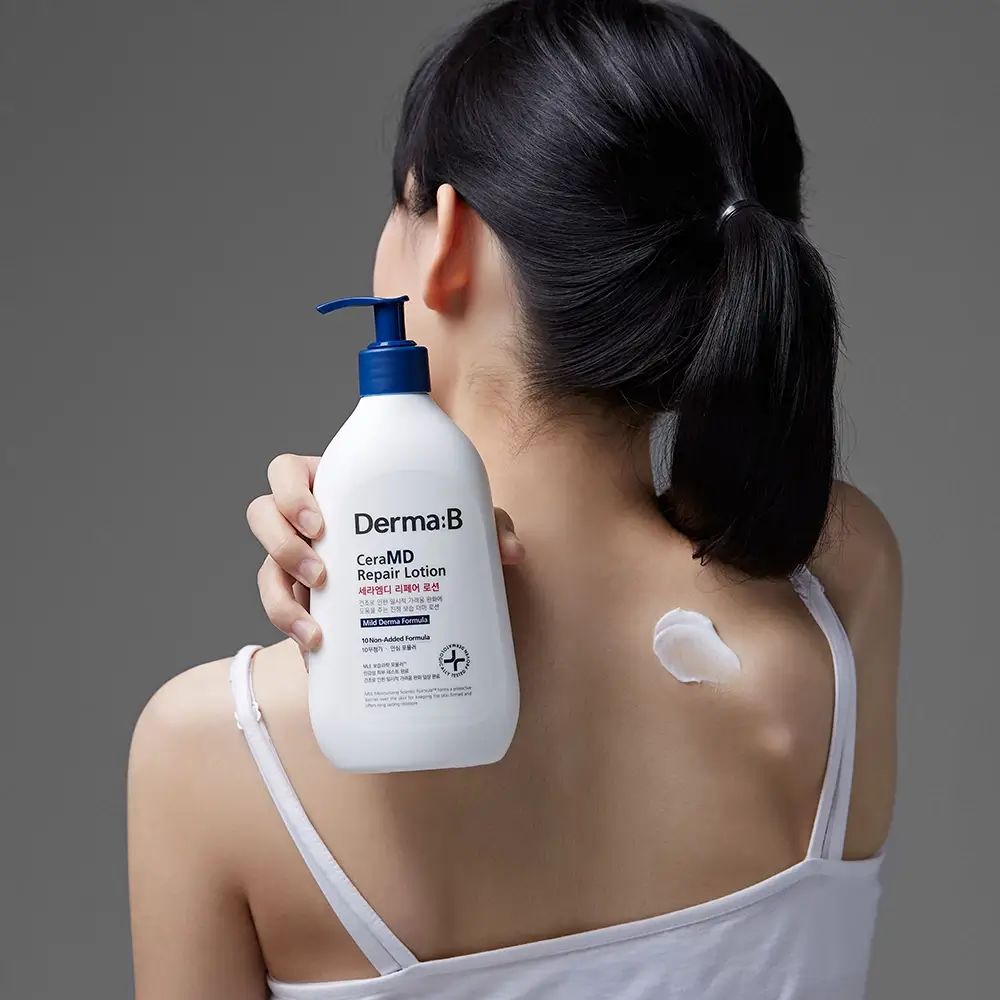 Frau hält eine weiße Flasche mit blauem Pumpkopf. Aufschrift: Derma:B CeraMD Repair Lotion. Klecks Lotion auf dem Rücken.