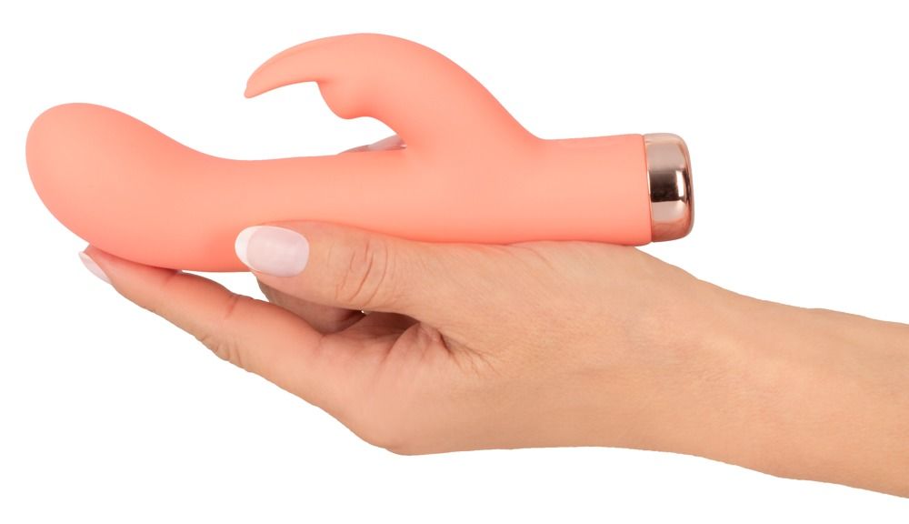 Eine Hand hält einen pfirsichfarbenen Mini-Rabbit-Vibrator mit gebogenem Schaft und kleinerer Spitze.