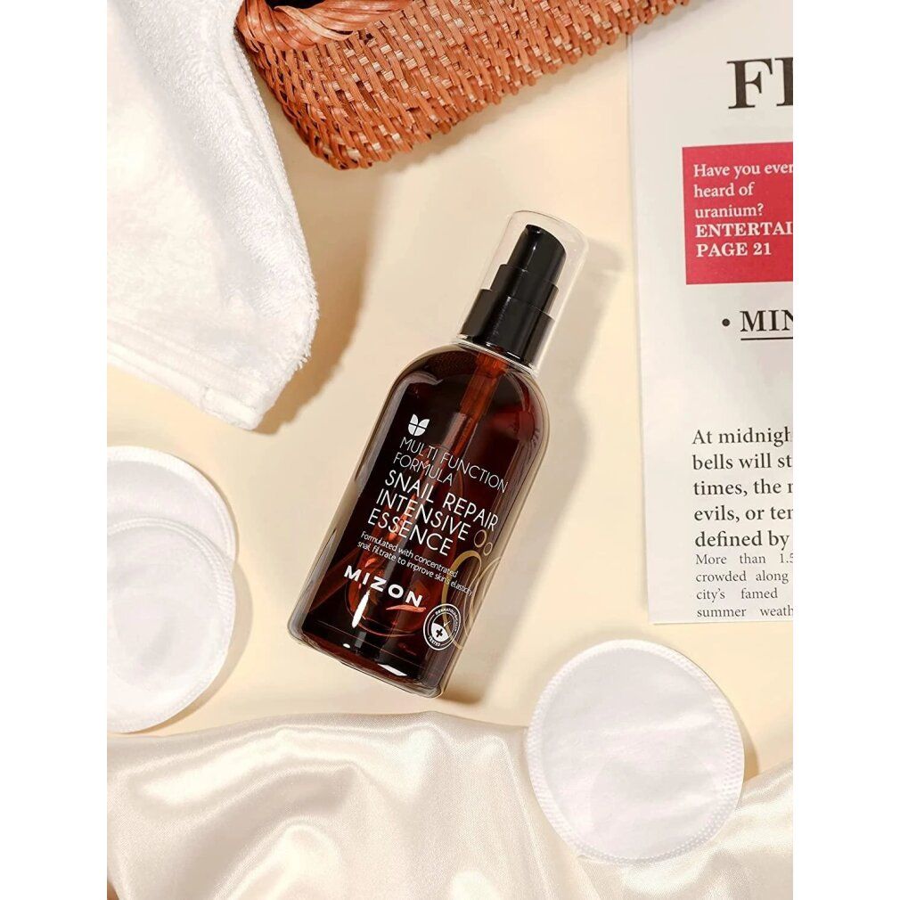 Produktflasche, Wattepads, Handtuch und Zeitschrift. Aufschrift: Snail Repair Intensive Essence. Marke: MIZON.