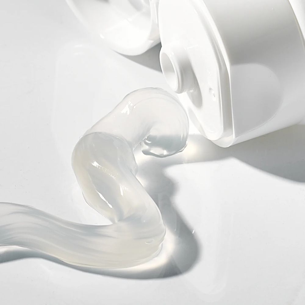 Zahnpasta-Strang, transparent, auf weißem Untergrund. Tube im Hintergrund.