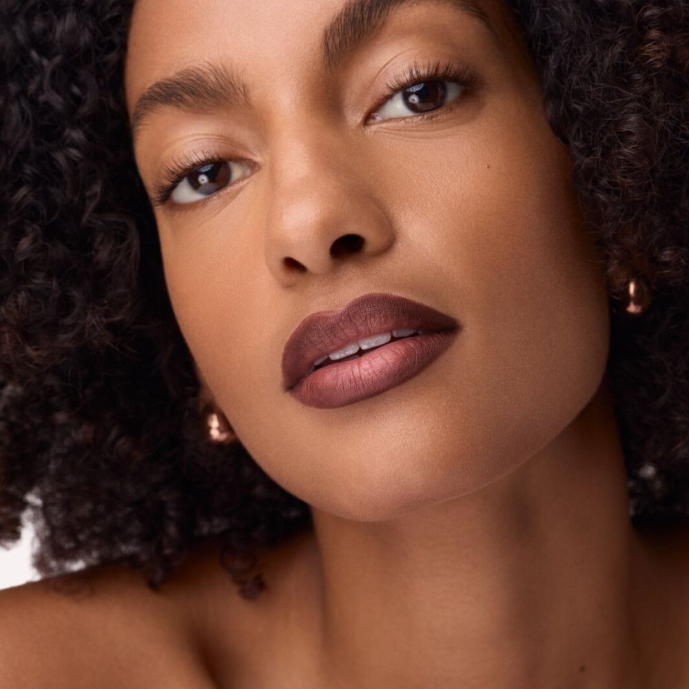 Porträt einer Frau mit braun geschminkten Lippen. Sieht direkt in die Kamera.