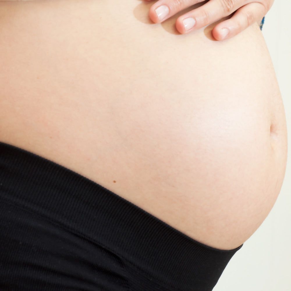 Schwarze Umstandshose, eng anliegend, hoher Bund. Bauchansicht, Hand auf dem Bauch.