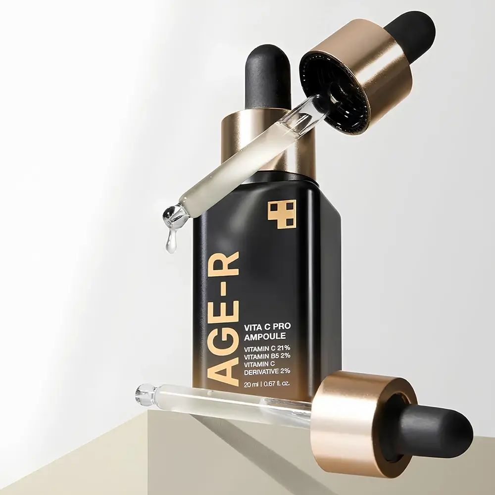 Dunkle Flasche mit goldener Kappe und Pipette. Zwei Pipetten liegen daneben. Aufschrift AGE-R und Vita C Pro Ampulle.