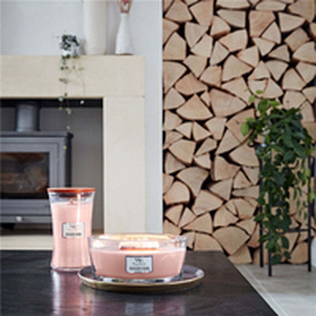 Zwei Kerzen auf einem Tisch. Eine hohe und eine breite, beide rosa. Holzstapel im Hintergrund.
