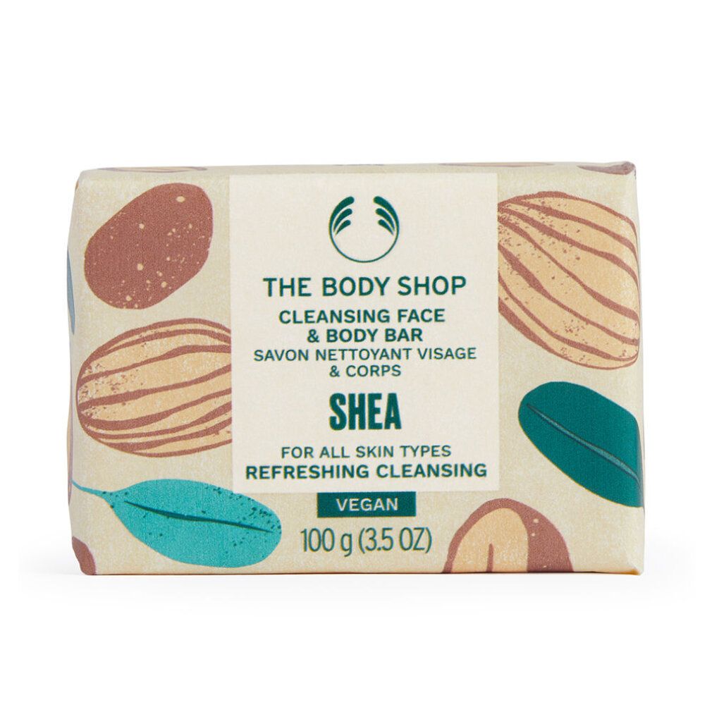 Verpackte Seife. Aufschrift: The Body Shop, Cleansing Face & Body Bar, Shea, Vegan. 100 g. Mit braunen und grünen Mustern.