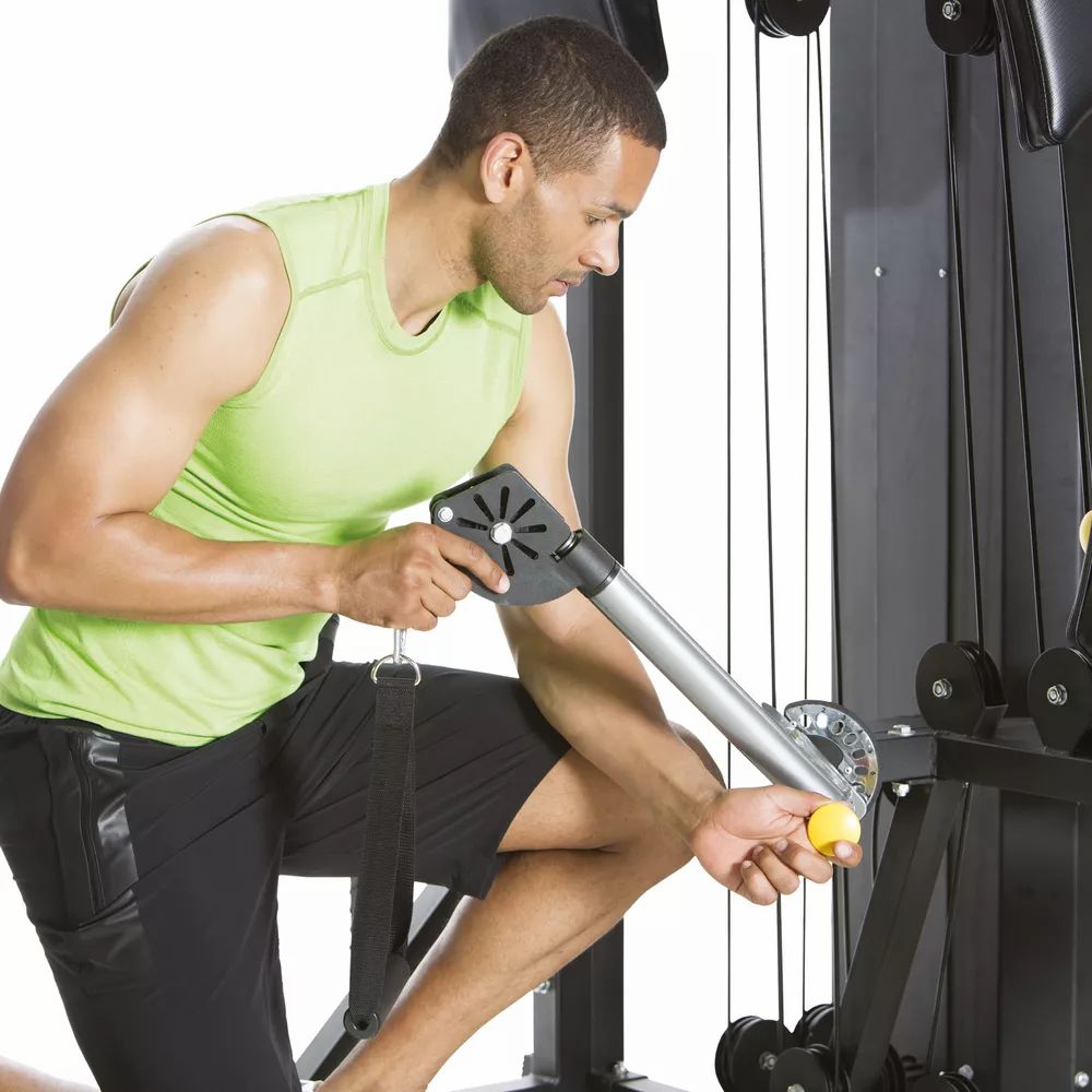 Mann trainiert an der Fitnessstation. Er hält einen Griff. Seilzüge und gelbe Verstellknöpfe. Horizon Fitness Torus 5.