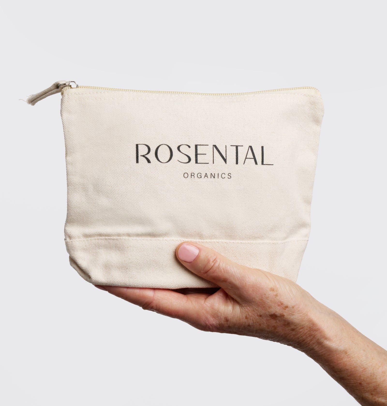 Beige Kosmetiktasche mit Reißverschluss, gehalten von einer Hand. Aufschrift: ROSENTAL ORGANICS.
