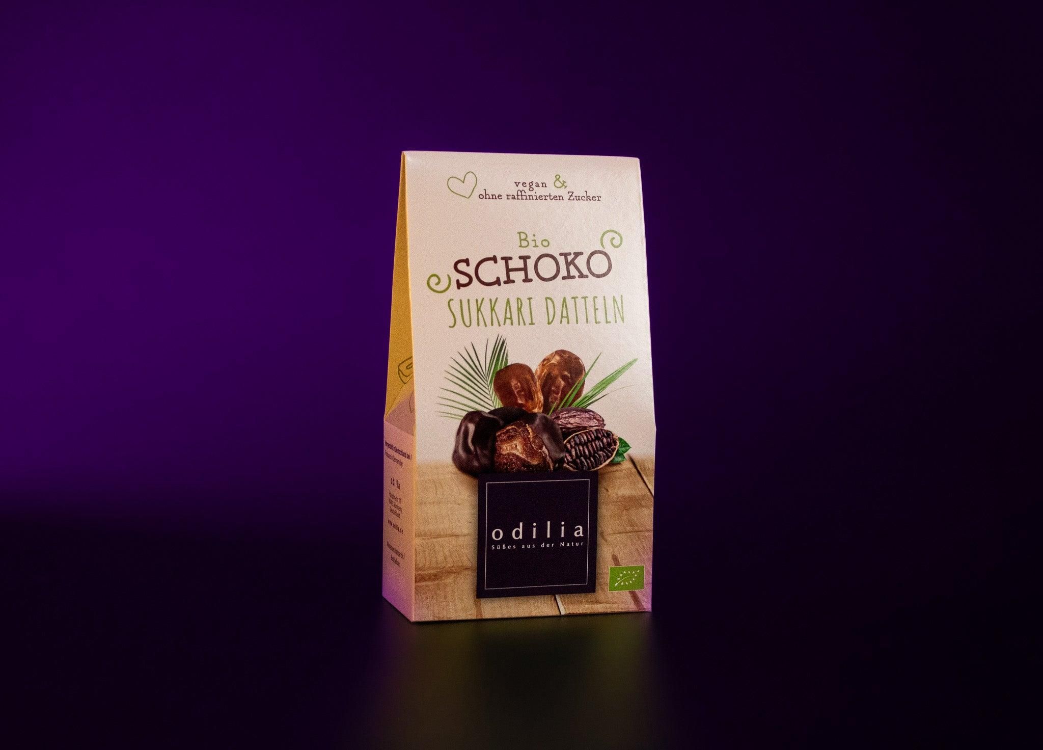 Verpackung mit Bio Schoko Sukkari Datteln, Odilia Marke, mit Datteln und Palmblatt-Illustration.