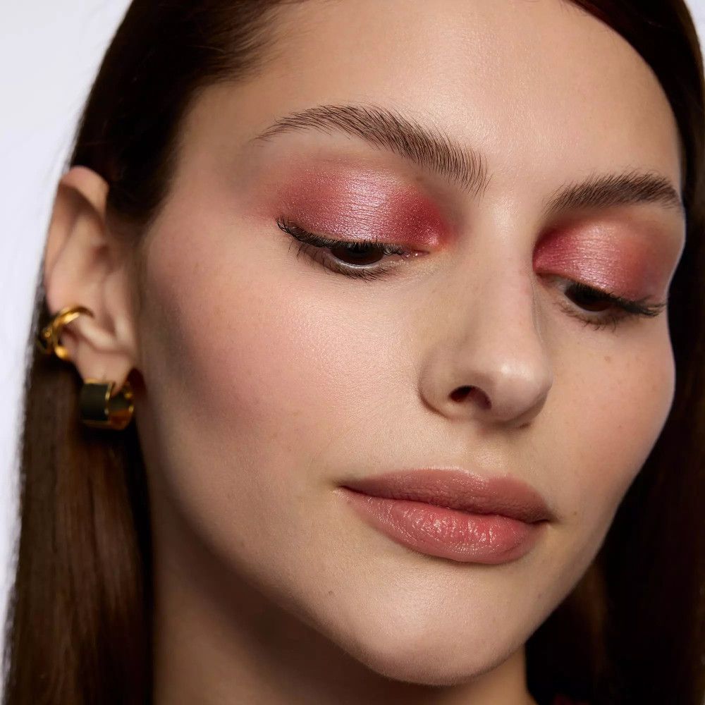 Nahaufnahme eines Gesichts mit rosa Lidschatten. Goldene Ohrringe.