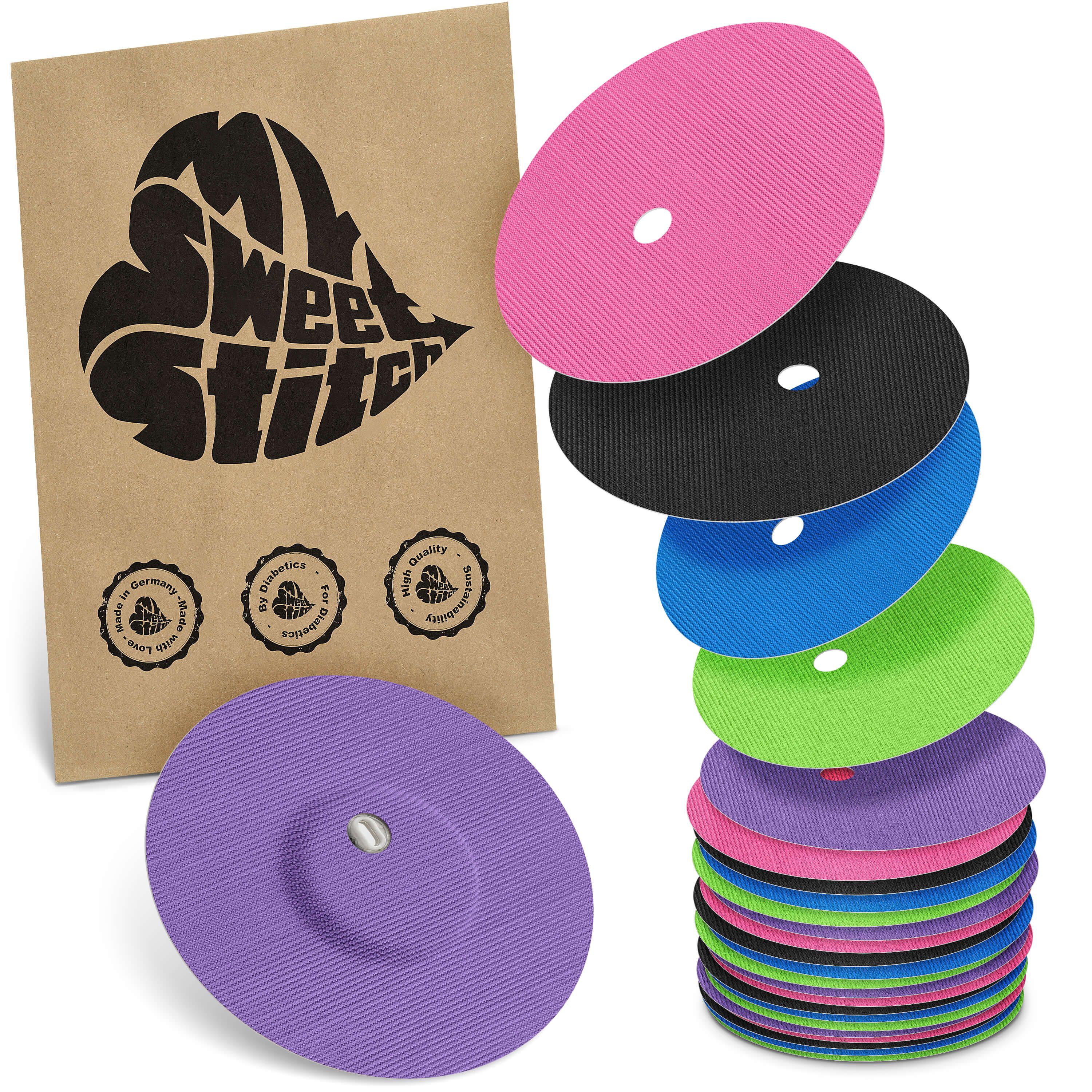 Packung mit Fixierpflastern. Mehrere farbige, runde Pflaster mit Loch und Aufkleber. Braune Verpackung mit Logo.