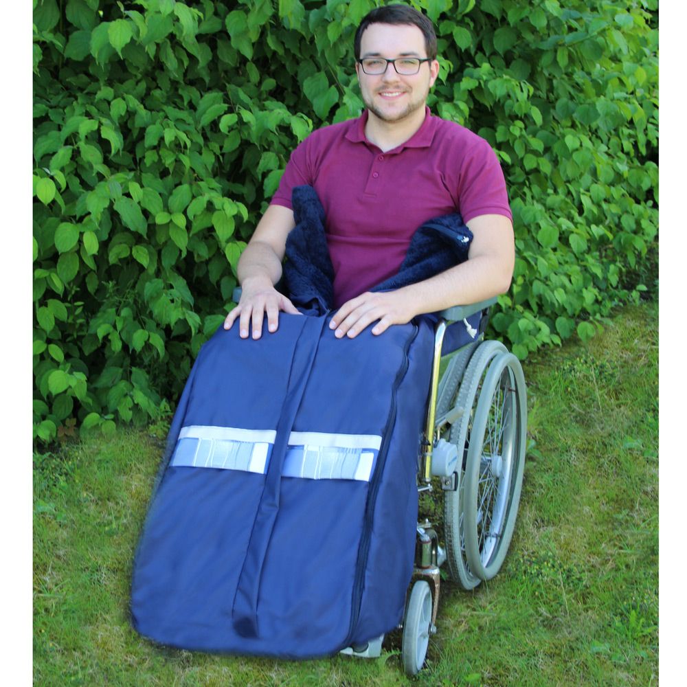 Blauer Sommerschlupfsack mit Querstreifen, an Rollstuhl befestigt. Mann im Rollstuhl. Grünpflanzen im Hintergrund.