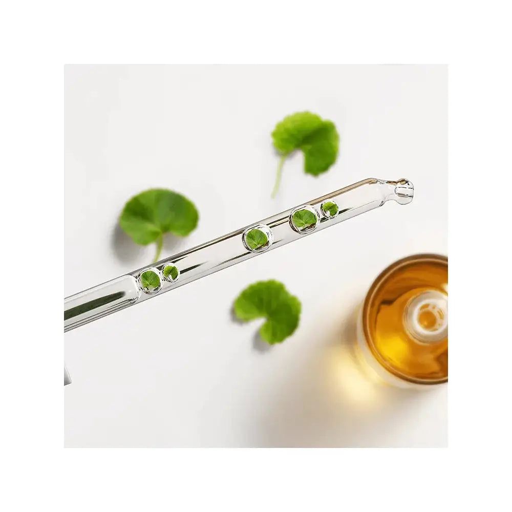 Pipette mit Tropfen gelber Flüssigkeit und grünen Blättern, neben einer Glasflasche.