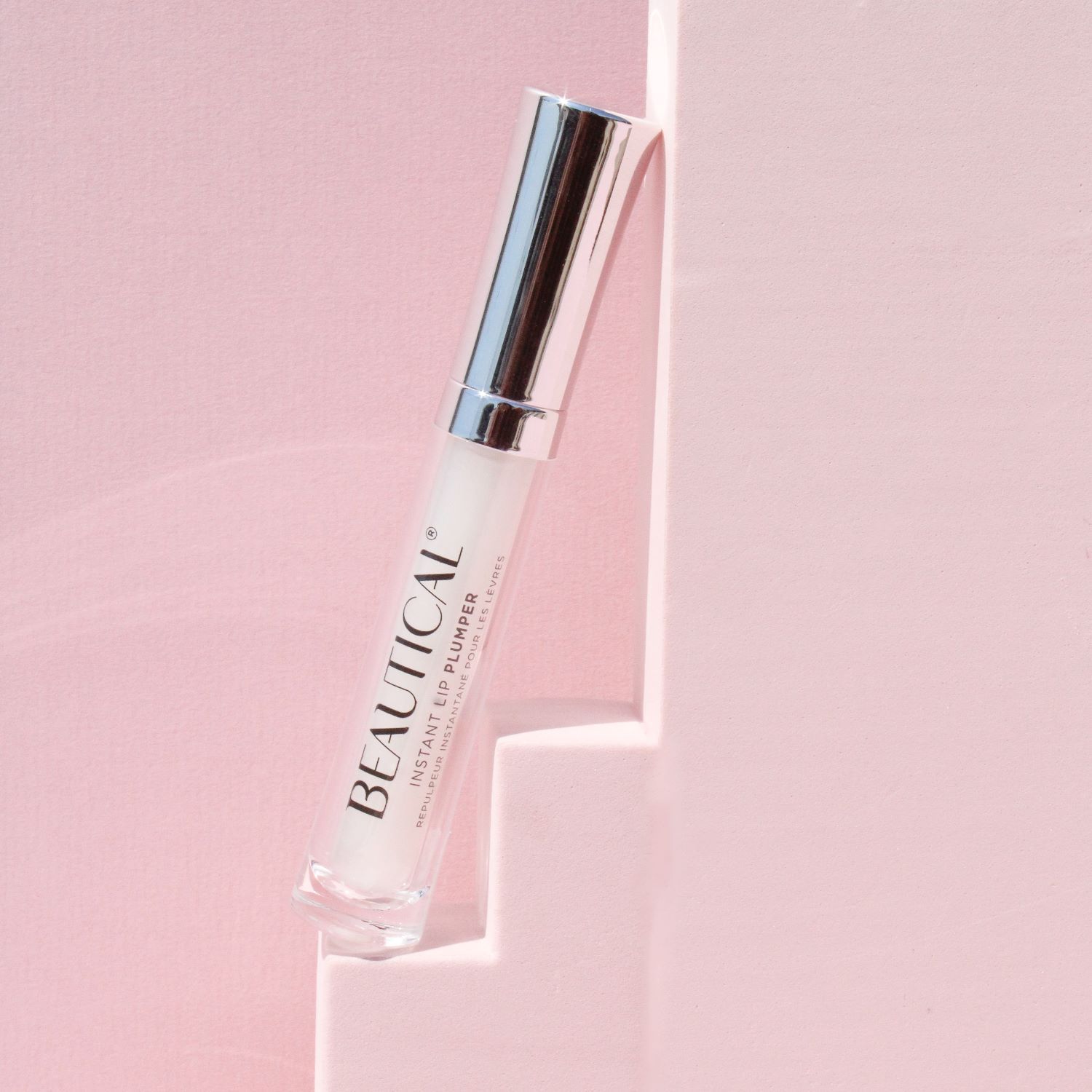 BEAUTICAL Instant Lip Plumper. Tube mit silberner Kappe, lehnt an einer rosa Wand. Weißer Applikator.