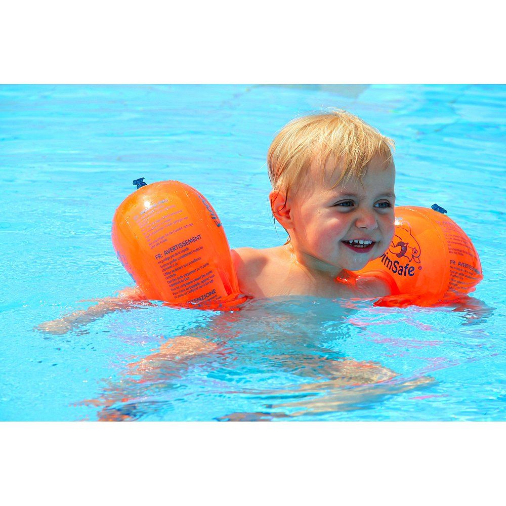 Kind im Schwimmbecken mit orangefarbenen Flipper SwimSafe Schwimmflügeln. Kind lächelt.