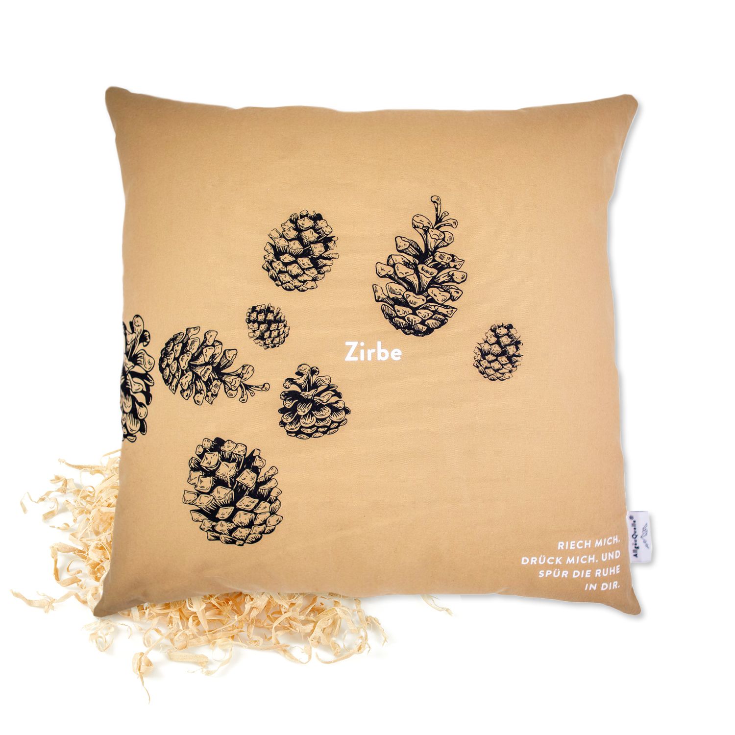 Beige Kissen mit Kiefernzapfen-Motiv. Text: Riech mich, drück mich, und spür die Ruhe in dir. Holzspäne daneben.