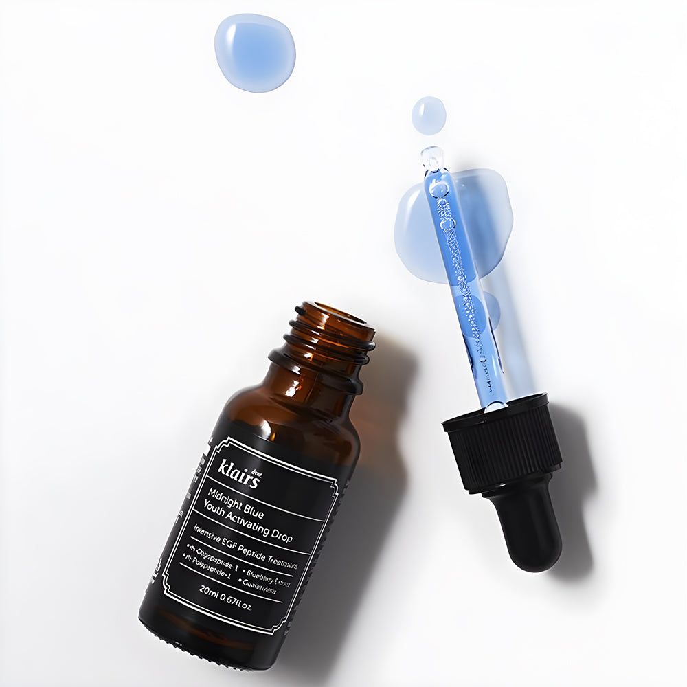 Braune Glasflasche mit schwarzem Deckel und Pipette. Blaue Flüssigkeit und Tropfen daneben. Etikett mit Text.