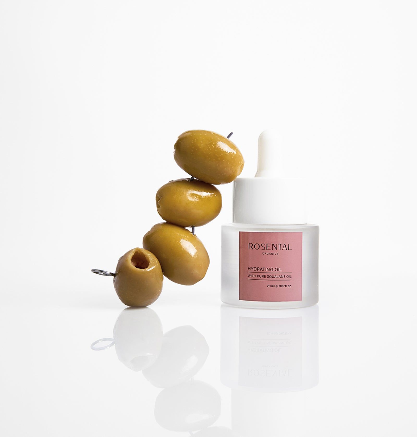 Glasflasche mit Oliven und Spieß. Weißer Hintergrund. Rosa Etikett mit Text.