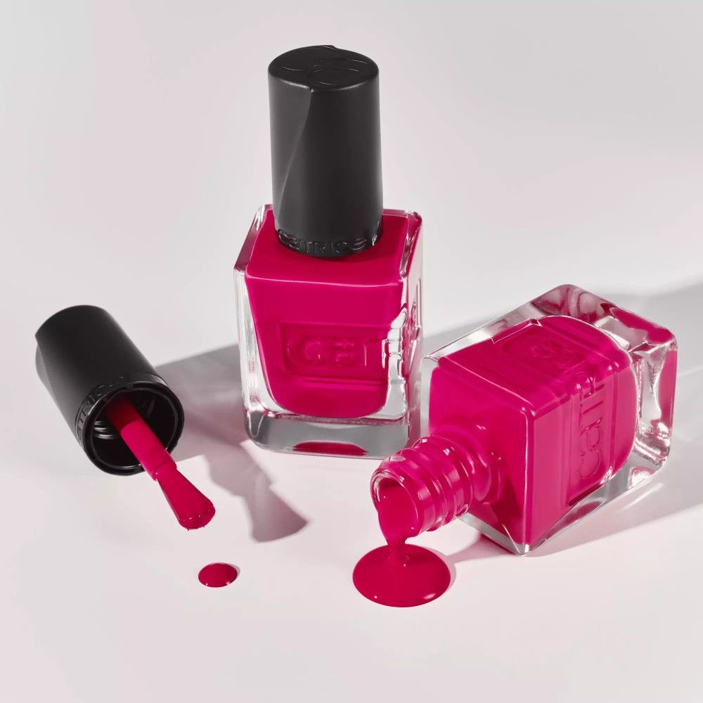 Zwei Nagellackflaschen, eine umgekippt, Nagellack verschüttet. Rosa Farbe. Schwarze Deckel.