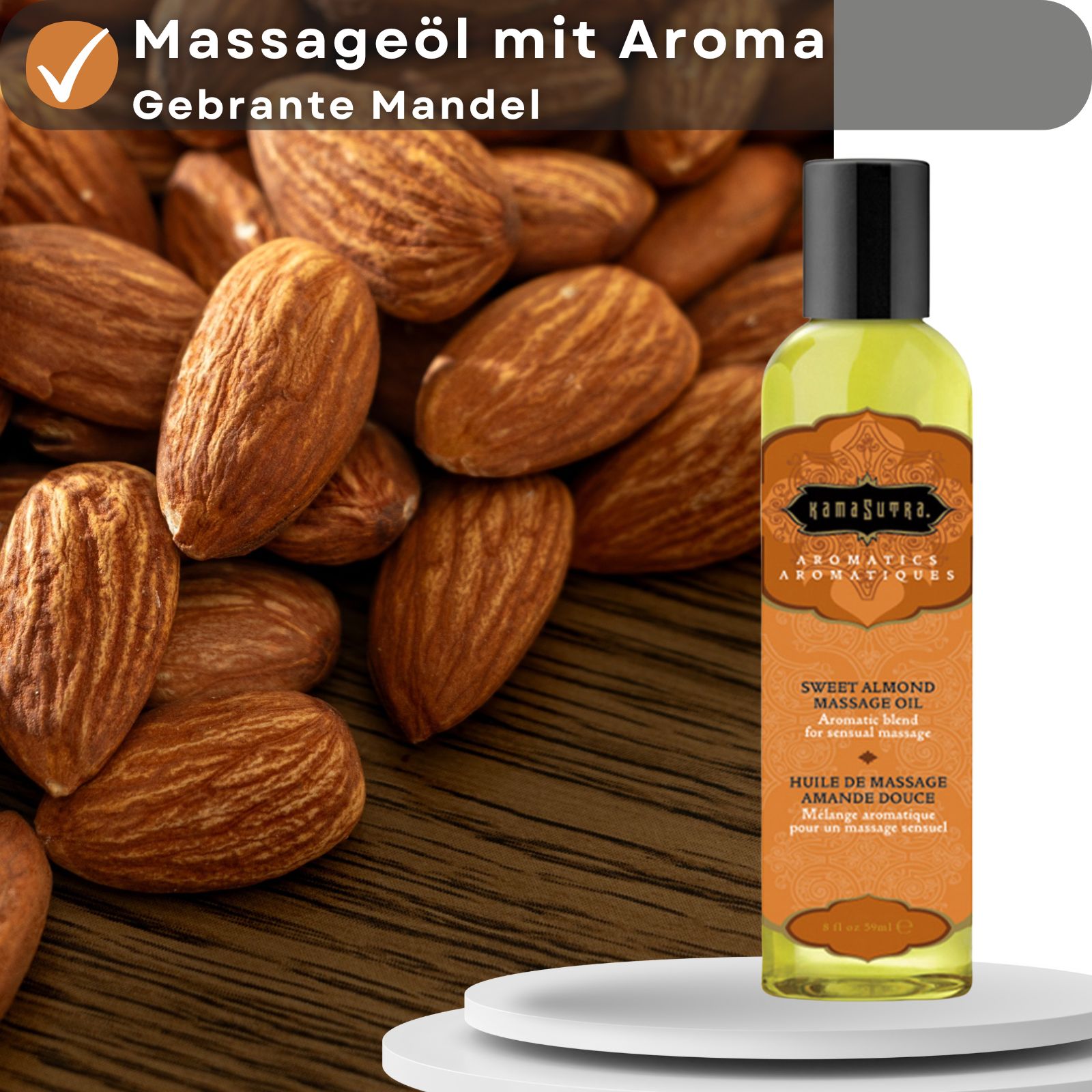 Massageöl-Flasche neben Mandeln und Text: Massageöl mit Aroma Gebrannte Mandel. Flasche steht auf einer weißen Plattform.