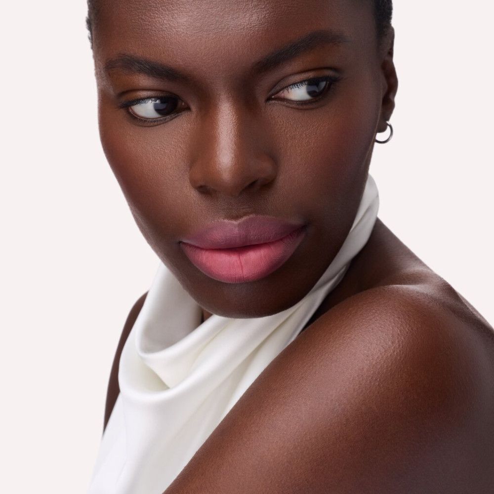 Porträt einer Person mit rosafarbenem Lippenstift. Person trägt ein weißes Oberteil.