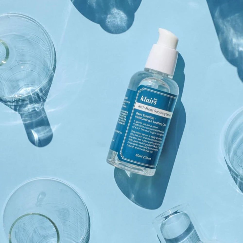 Klairs Rich Moist Soothing Serum. Flasche auf blauem Hintergrund mit Glasgefäßen.